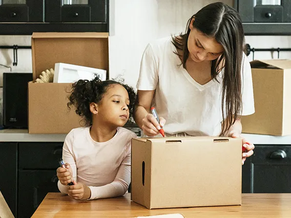 A mother and her young daughter labeling a moving box