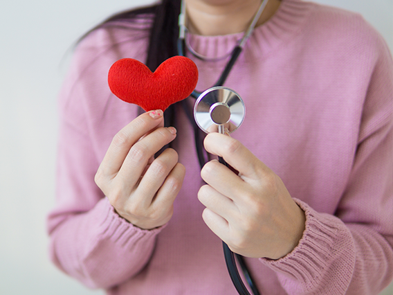 Woman wearing a pink sweater holding a stethoscope up next to a small red felt heart