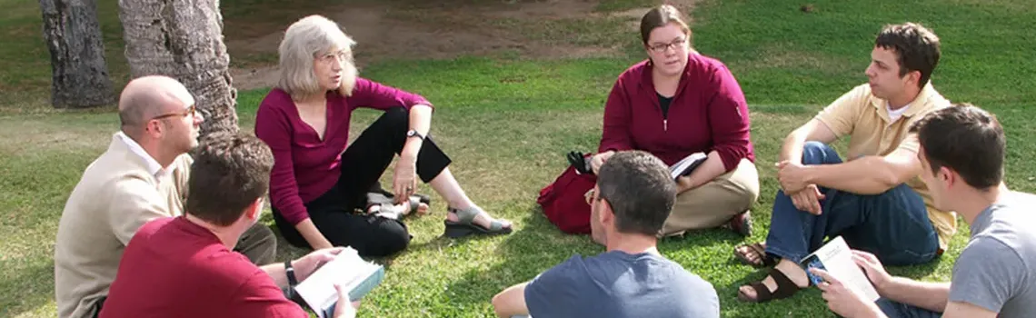 Group of faculty sitting on grass talking